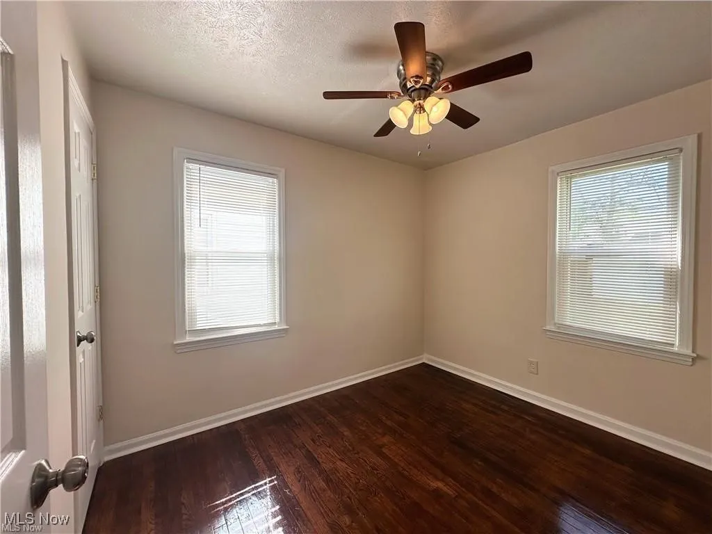 Empty room featuring dark wood-style floors, a textured ceiling, and a ceiling fan