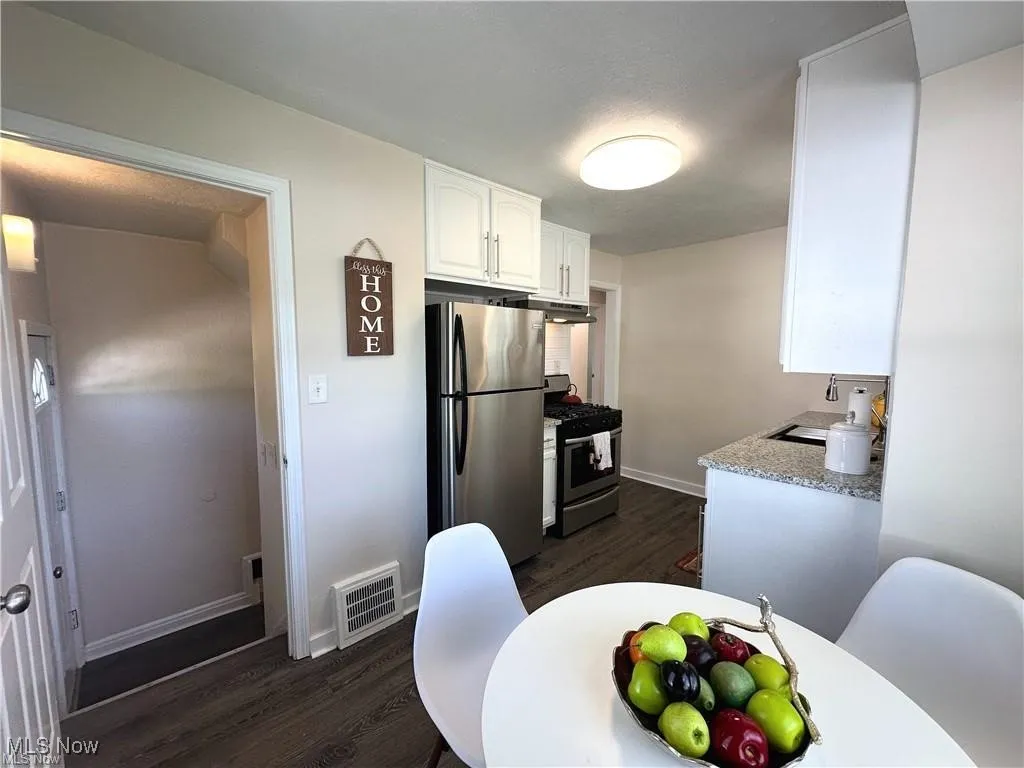 Kitchen featuring dark wood finished floors, stainless steel appliances, white cabinets, under cabinet range hood, and a textured ceiling