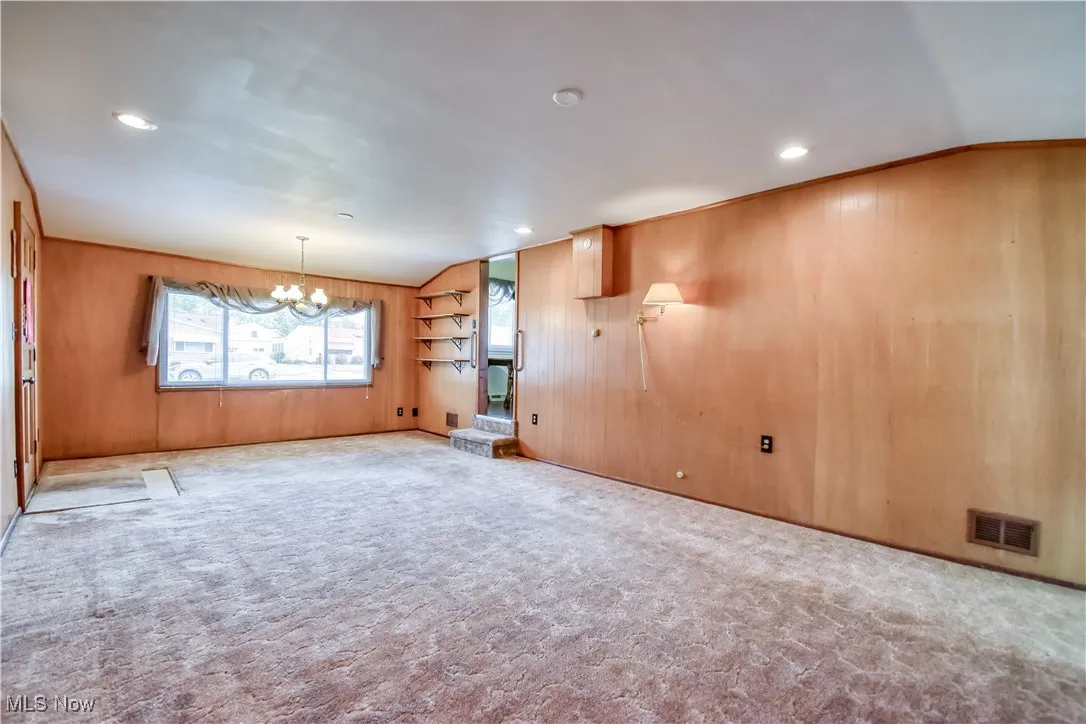 Spare room with wood walls, carpet flooring, a chandelier, and recessed lighting
