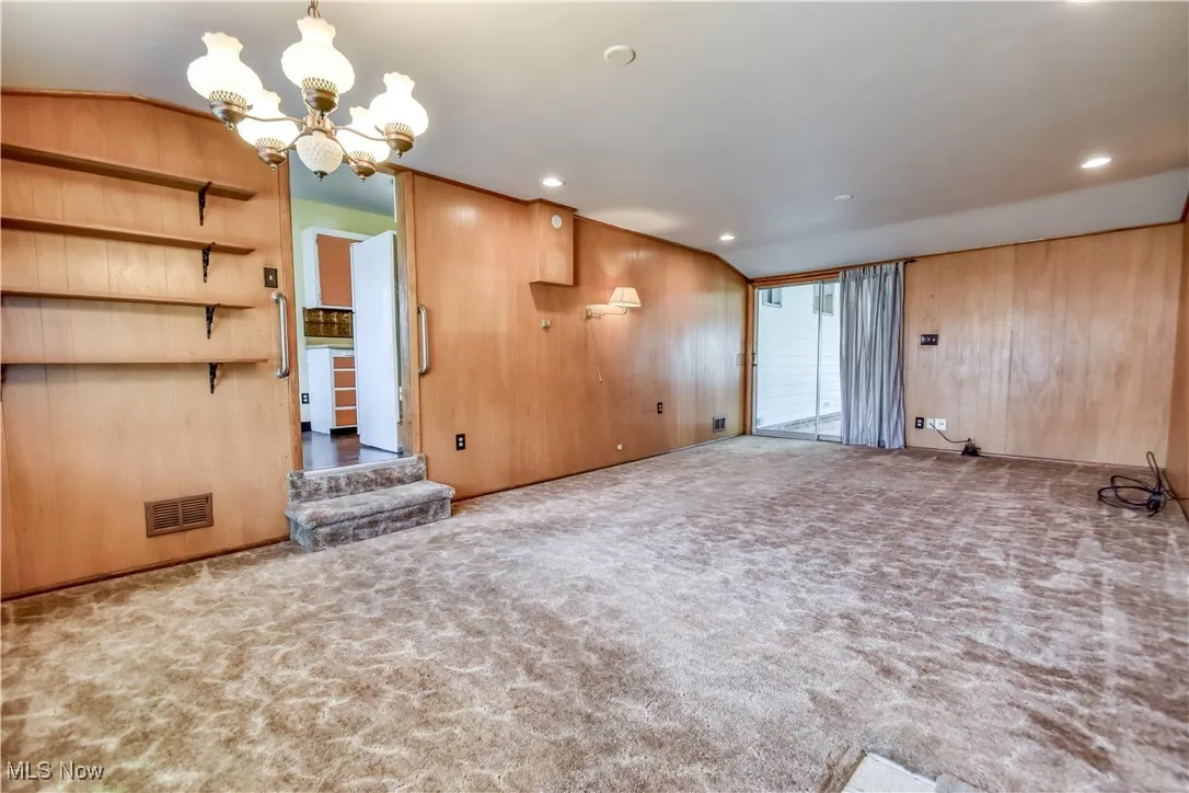 Unfurnished living room featuring carpet floors, a chandelier, wood walls, vaulted ceiling, and recessed lighting