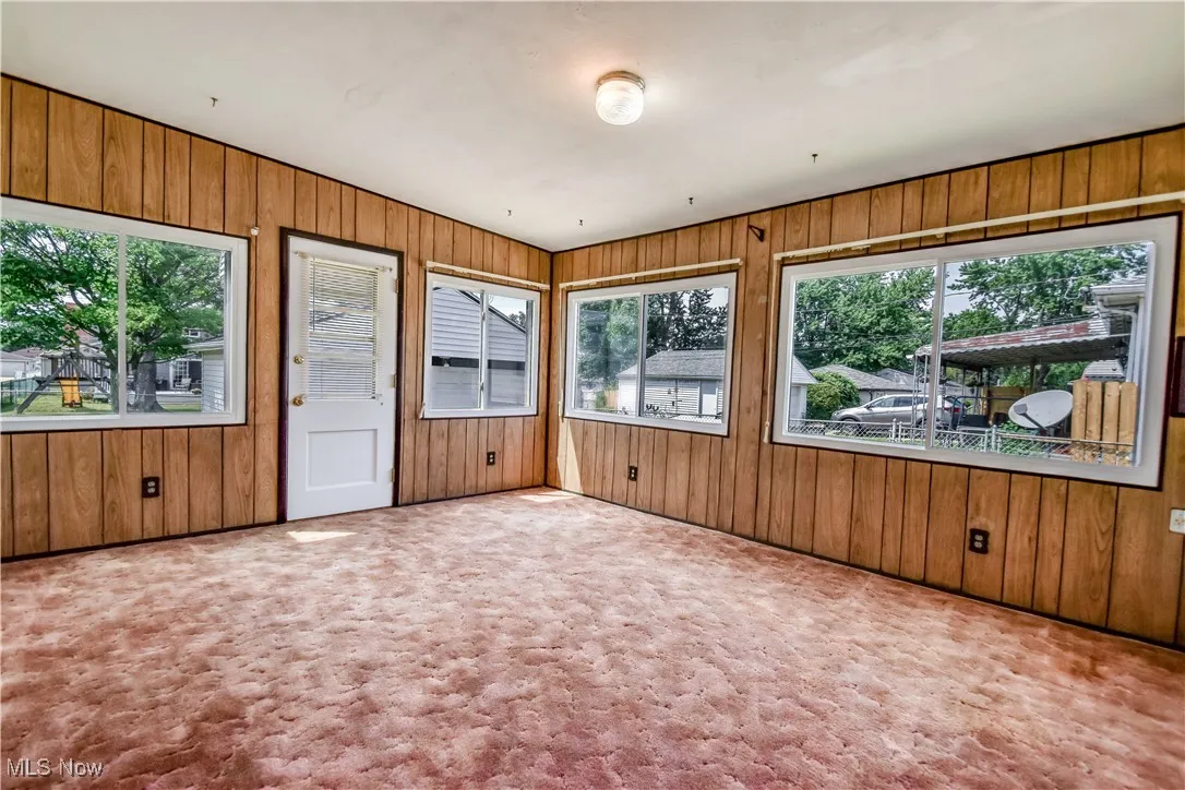 Unfurnished sunroom featuring plenty of natural light, carpet floors, and wood walls