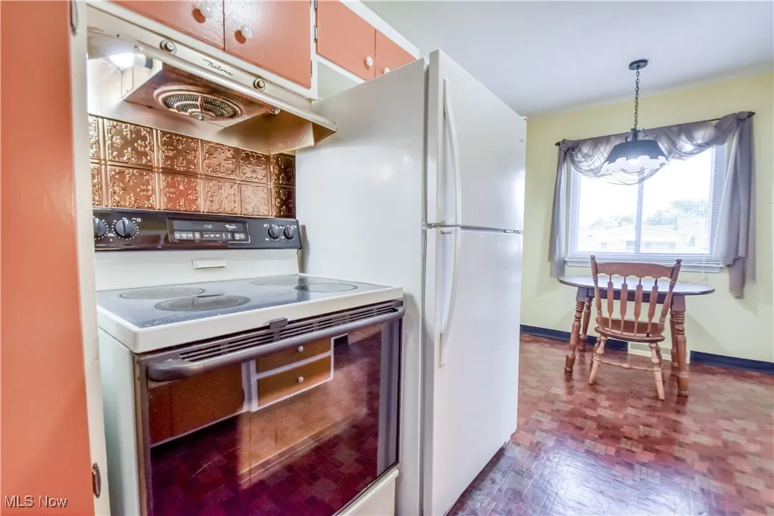 Kitchen featuring white electric range oven, under cabinet range hood, and pendant lighting