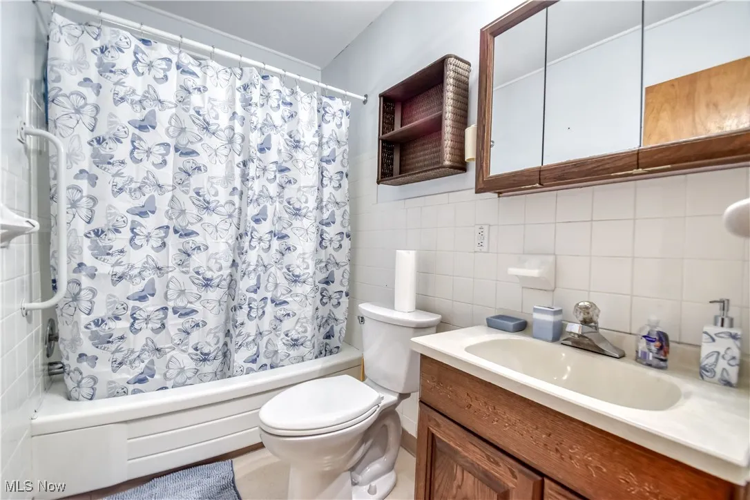 Bathroom featuring tile walls, shower / bath combination with curtain, vanity, and decorative backsplash