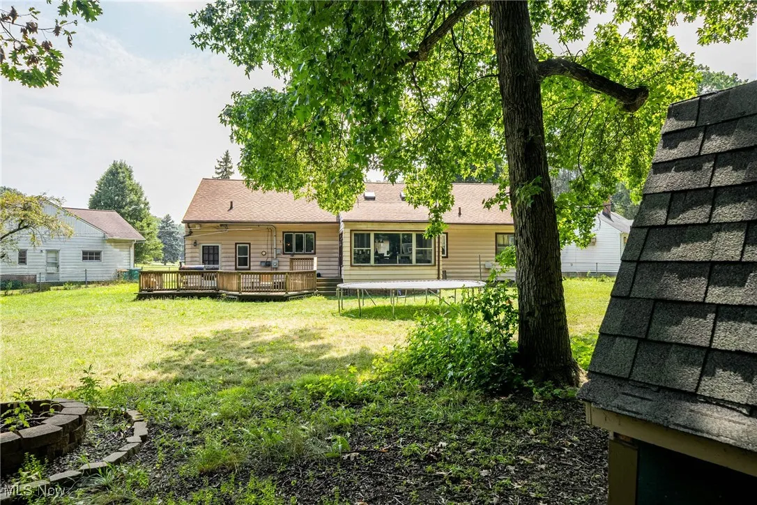 Back of house with a trampoline, a deck, and a lawn