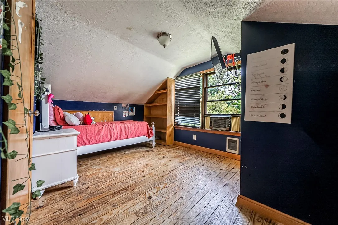 Bedroom with a textured ceiling, hardwood / wood-style floors, and vaulted ceiling