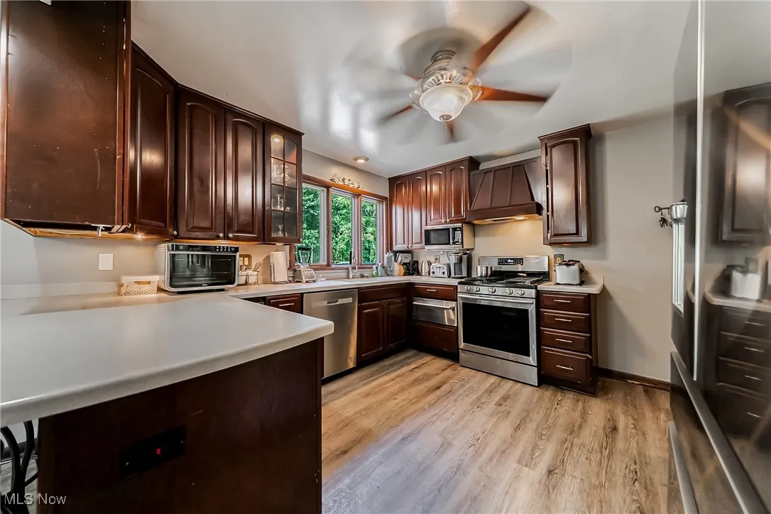 Kitchen featuring light wood-style flooring, stainless steel appliances, light countertops, glass insert cabinets, and dark brown cabinetry