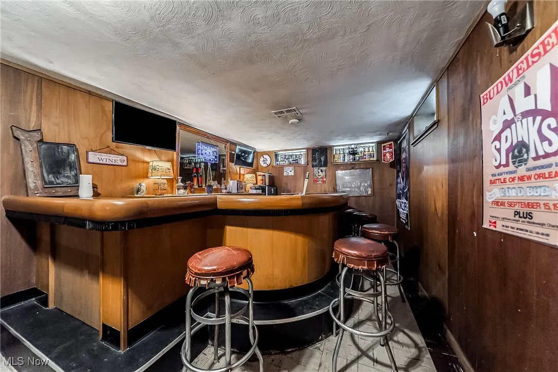 Indoor dry bar featuring wood walls and a textured ceiling