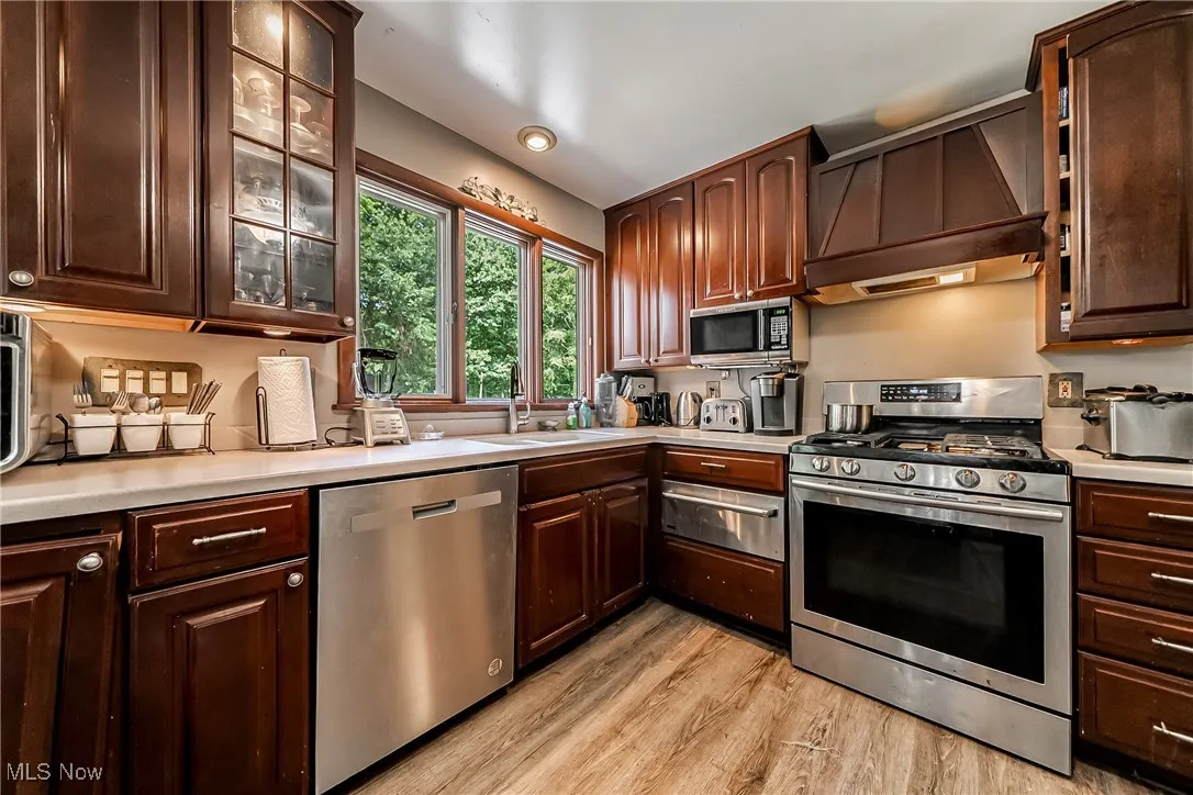 Kitchen with stainless steel appliances, light countertops, light wood-type flooring, dark brown cabinets, and a warming drawer