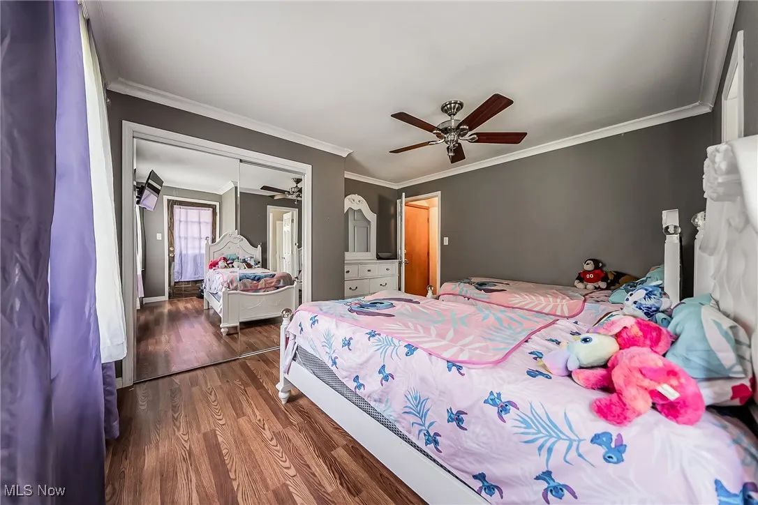 Bedroom with wood finished floors, crown molding, a closet, and a ceiling fan
