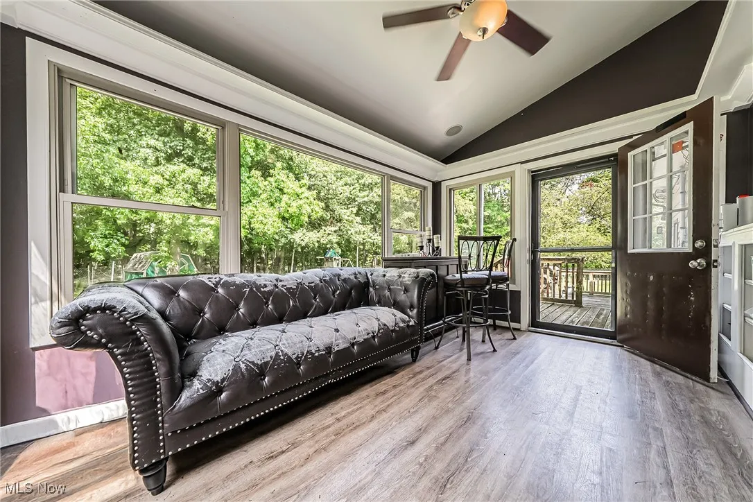 Sunroom / solarium with vaulted ceiling, wood finished floors, and view of scattered trees