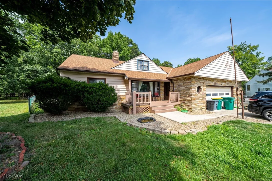 View of front of house featuring a chimney, a front yard, stone siding, an attached garage, and a shingled roof