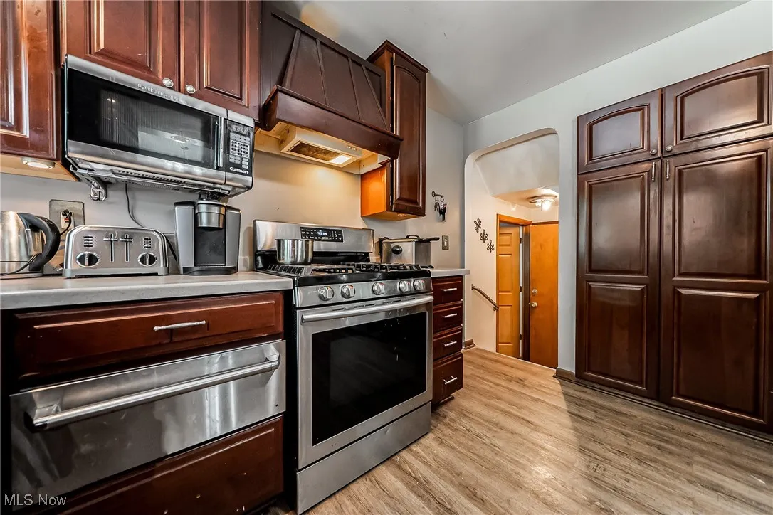 Kitchen featuring a warming drawer, stainless steel appliances, premium range hood, light countertops, and light wood-style flooring