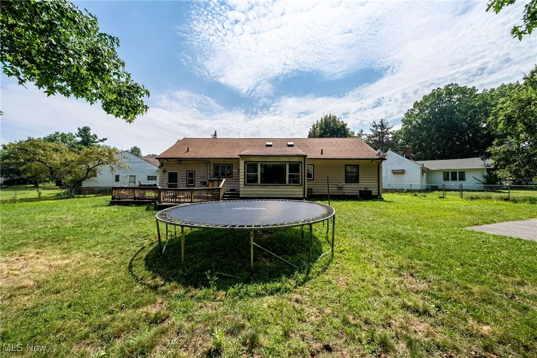 Rear view of house featuring a fenced backyard, a trampoline, and a wooden deck