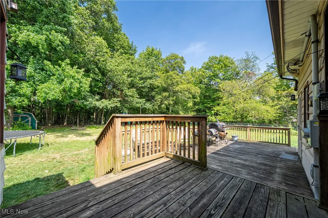 Wooden deck featuring a trampoline, a lawn, and view of wooded area