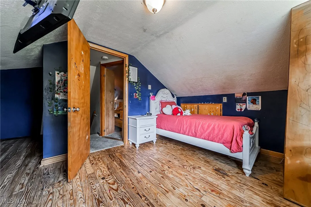 Bedroom featuring a textured ceiling, wood finished floors, and lofted ceiling