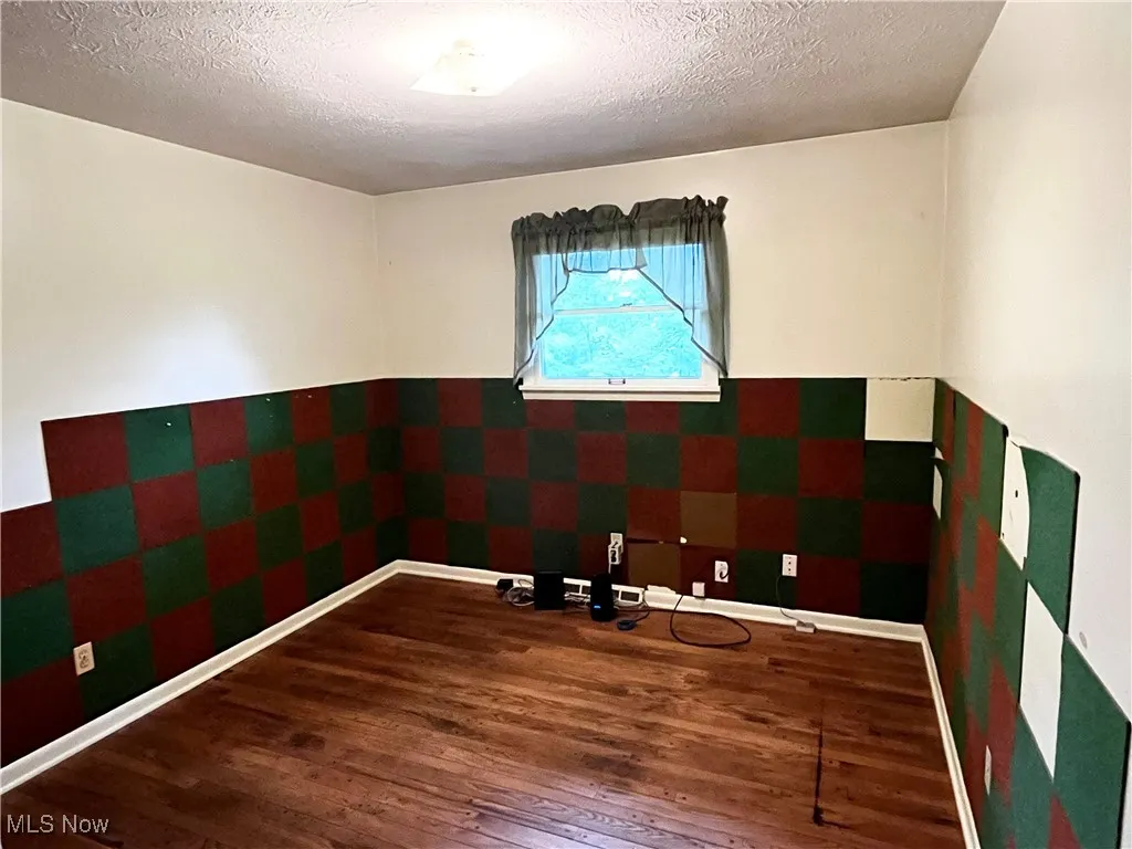 Unfurnished room with wood finished floors, a textured ceiling, and wallpapered walls