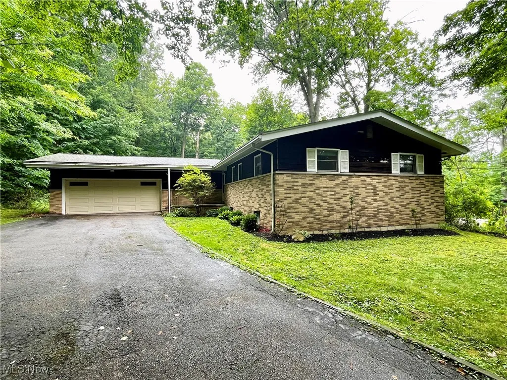 View of front of property featuring a garage, asphalt driveway, brick siding, and a front lawn