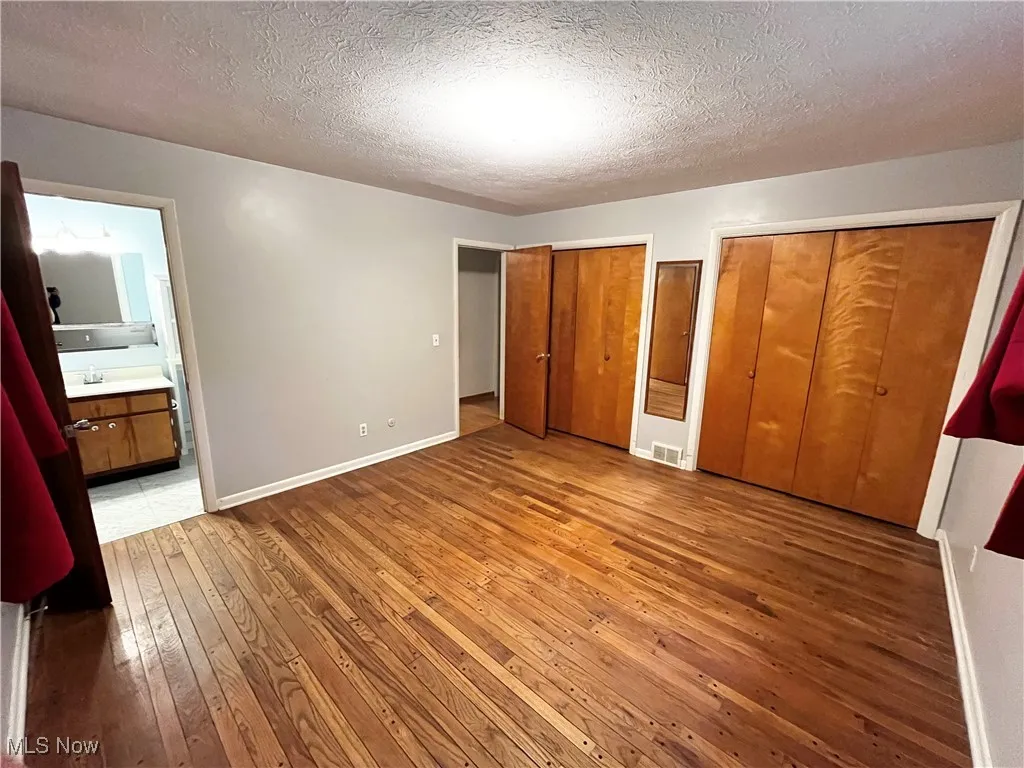 Unfurnished bedroom with multiple closets, a textured ceiling, light wood-type flooring, and ensuite bath