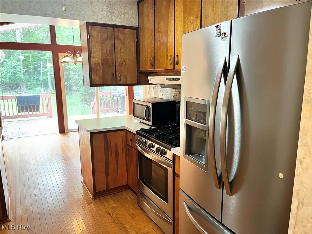 Kitchen with stainless steel appliances, light wood finished floors, a peninsula, light countertops, and brown cabinetry