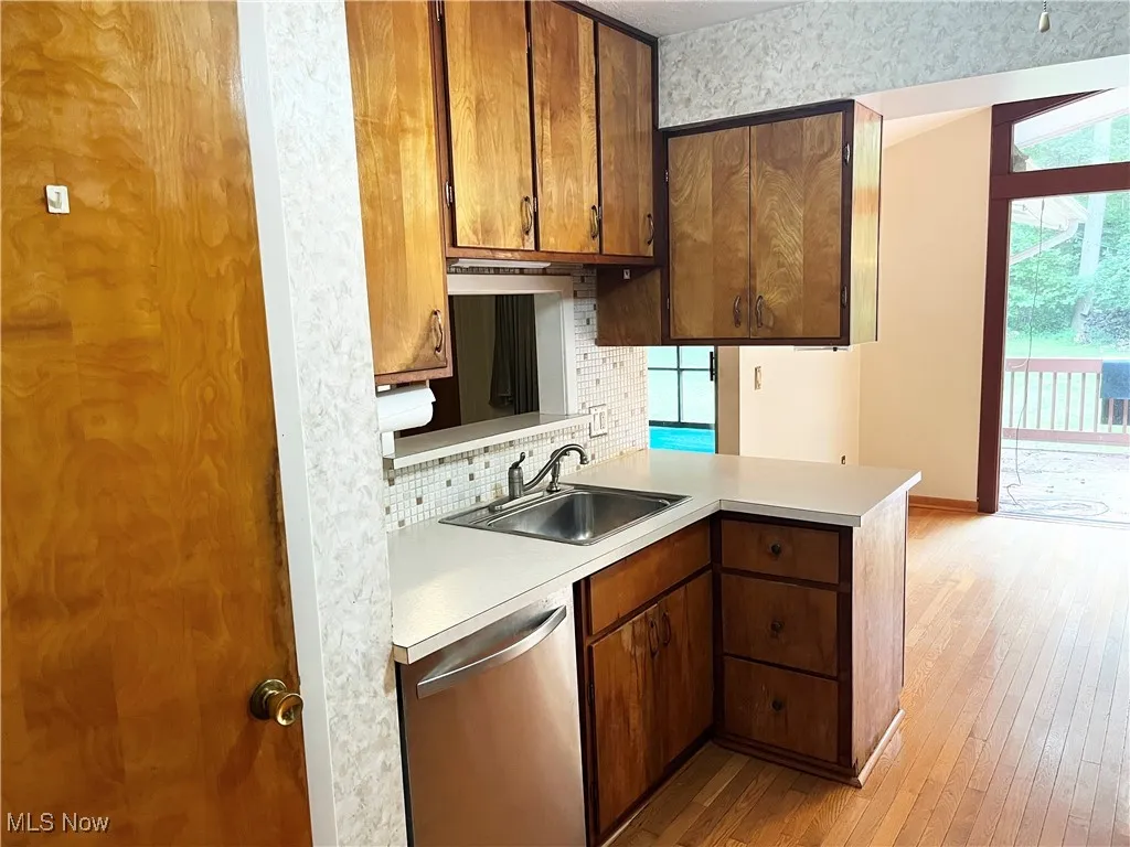 Kitchen with light countertops, backsplash, stainless steel dishwasher, and light wood-type flooring