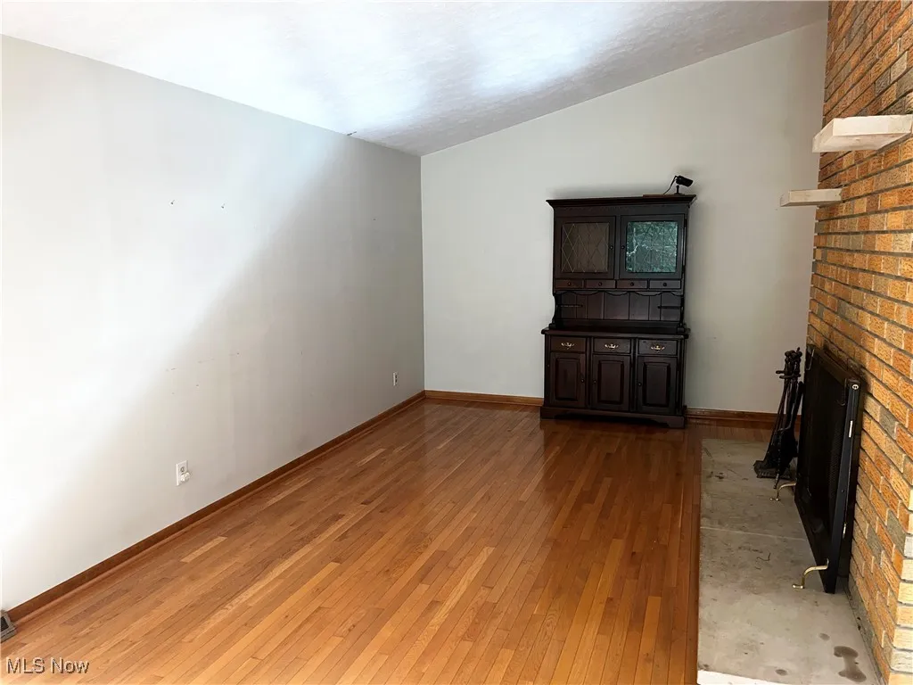 Unfurnished living room featuring vaulted ceiling, light wood finished floors, and a fireplace