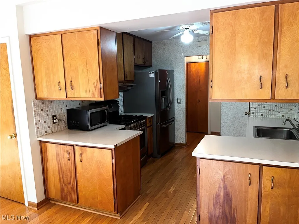 Kitchen with tasteful backsplash, light wood-style floors, gas range, and a ceiling fan
