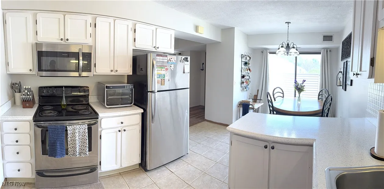 Kitchen featuring appliances with stainless steel finishes, light countertops, a textured ceiling, a chandelier, and white cabinets