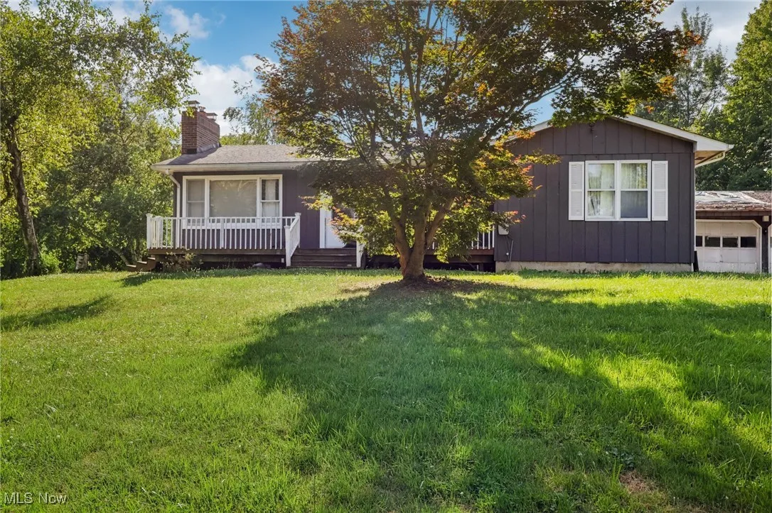 Ranch-style home with a garage, a chimney, a front yard, a deck, and board and batten siding