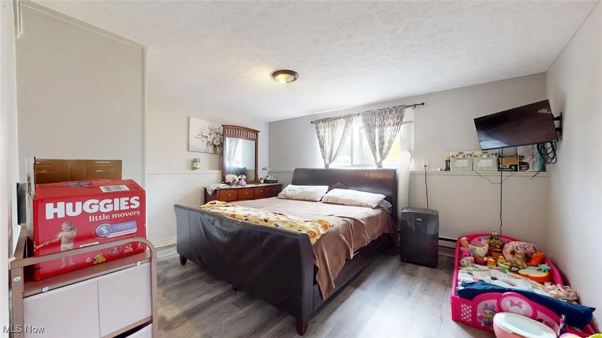 Bedroom with wood finished floors, a textured ceiling, and baseboard heating