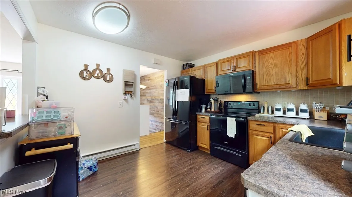 Kitchen with black appliances, tasteful backsplash, dark wood-style floors, baseboard heating