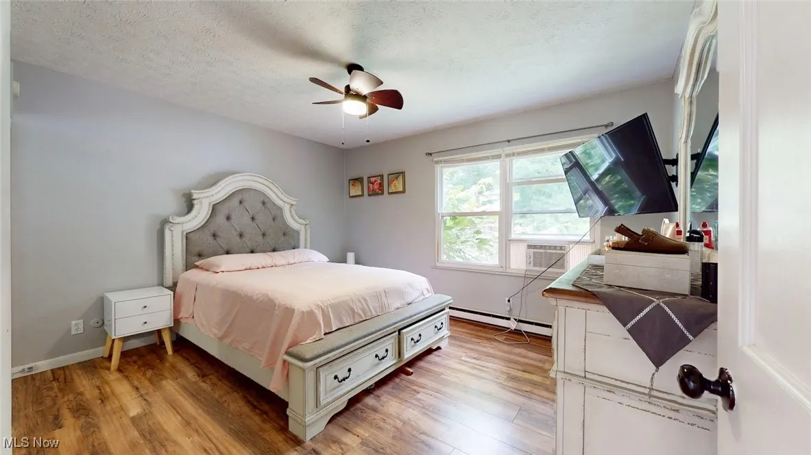 Bedroom featuring light flooring, a textured ceiling, baseboard heating, cooling unit, and ceiling fan