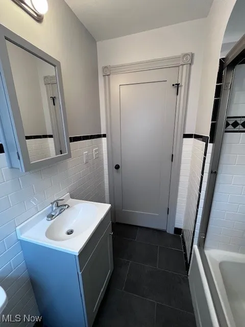 Full bath with tile walls, vanity, tile patterned flooring, and wainscoting