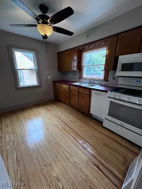 Kitchen with stove, a ceiling fan, dark countertops, and dishwashing machine