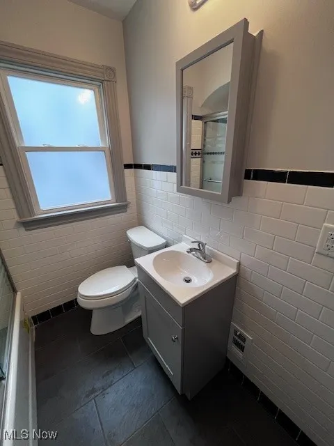 Bathroom with tile walls, a wainscoted wall, vanity, an enclosed shower, and tile patterned floors
