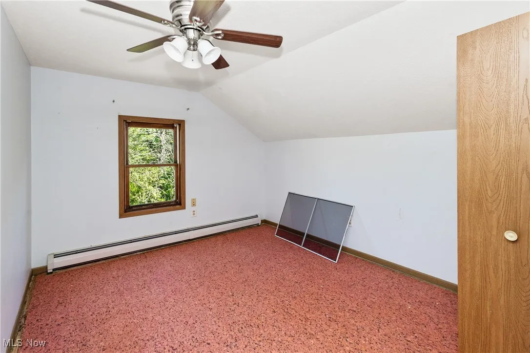 Additional living space with a baseboard heating unit, vaulted ceiling, and carpet floors