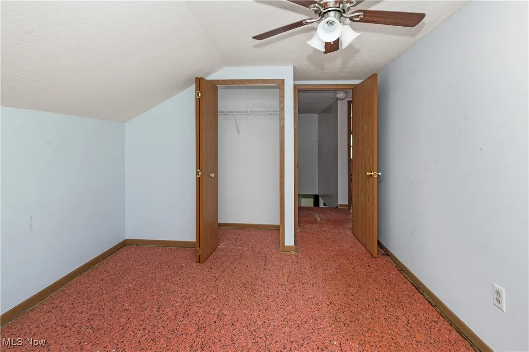 Unfurnished bedroom featuring a textured ceiling, a closet, vaulted ceiling, and ceiling fan