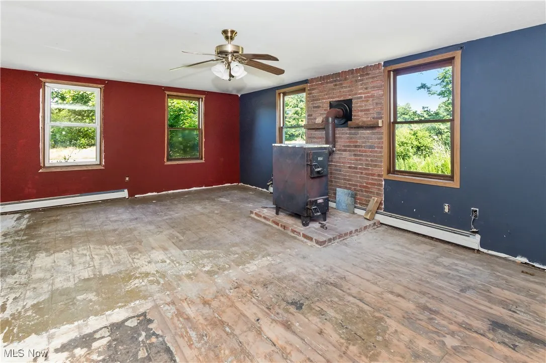 Unfurnished living room featuring a wood stove, a baseboard radiator, ceiling fan, and hardwood / wood-style floors