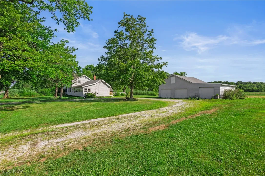 View of green lawn with driveway, an outbuilding, and a garage