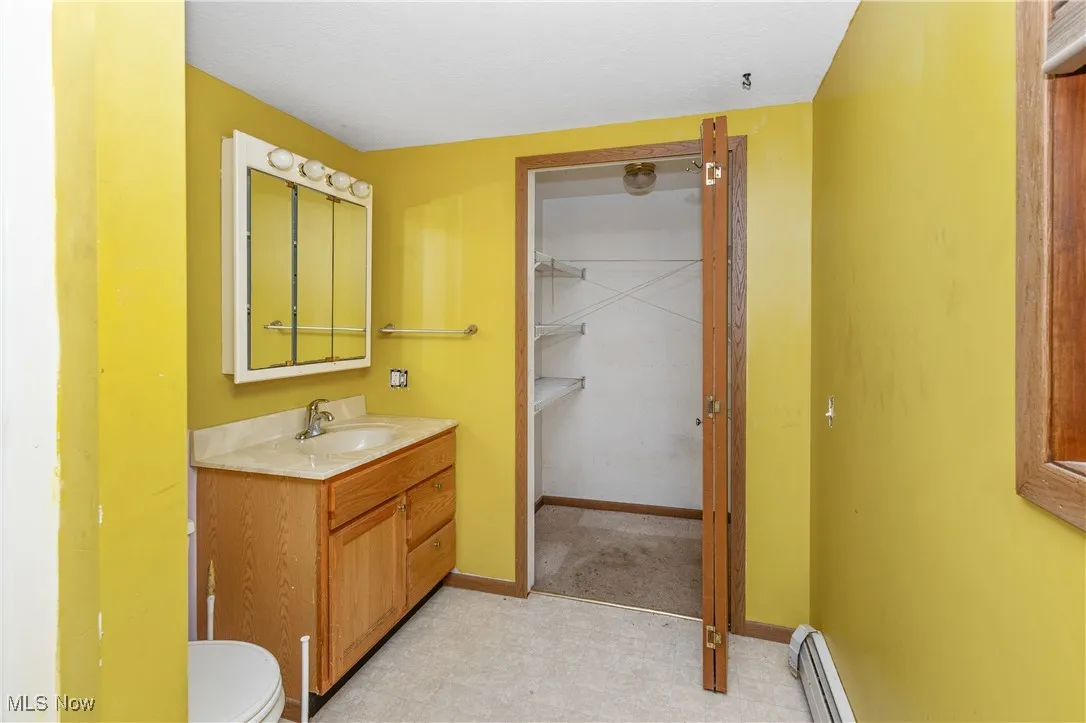 Bathroom featuring vanity, baseboard heating, a walk in closet, and tile patterned floors