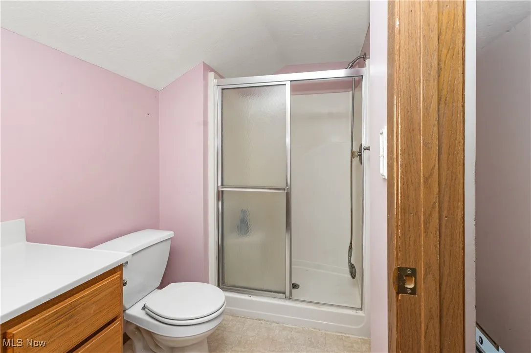 Full bathroom with lofted ceiling, a stall shower, vanity, and a textured ceiling