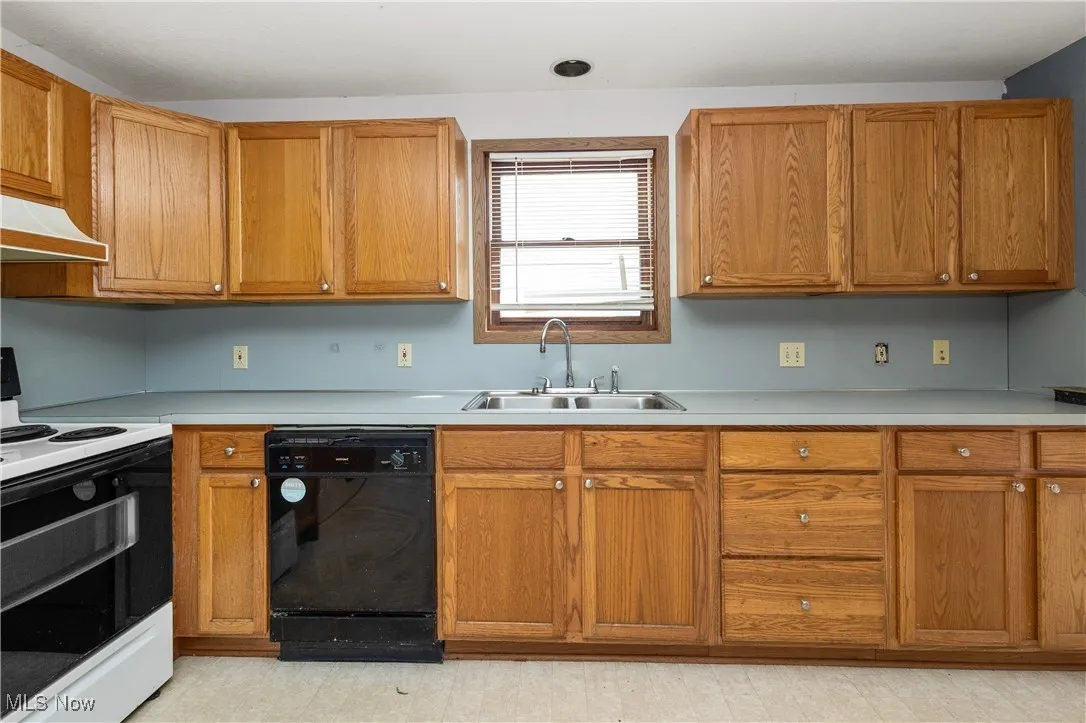 Kitchen with white range with electric stovetop, black dishwasher, light countertops, brown cabinets, and under cabinet range hood