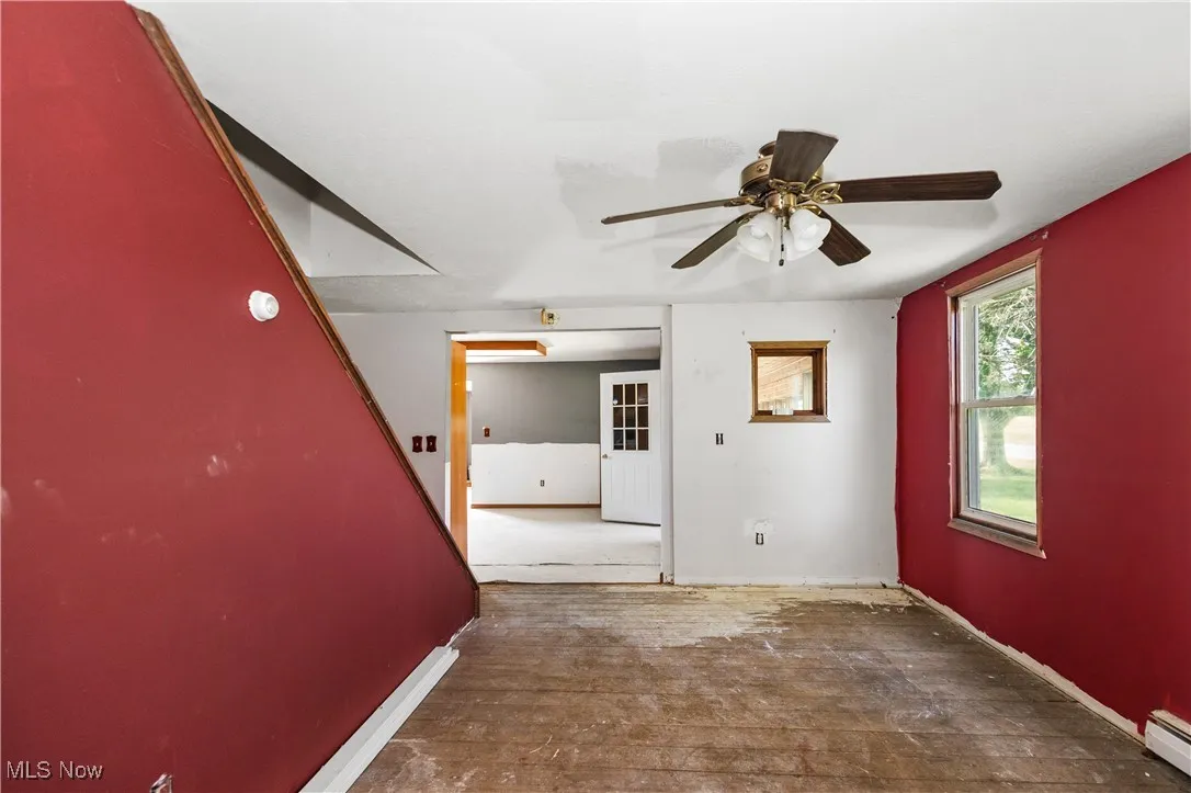 Unfurnished room featuring ceiling fan, wood-type flooring, and a baseboard heating unit