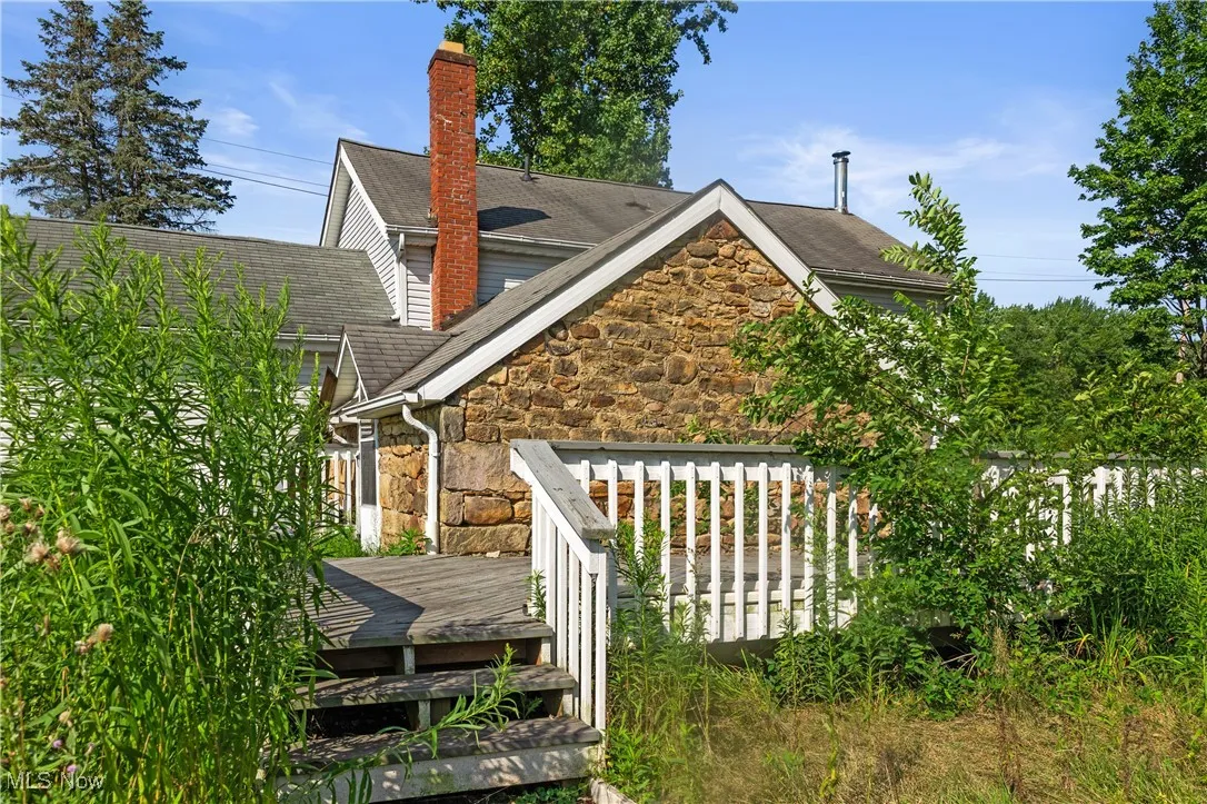 Back of property featuring stone siding, a chimney, roof with shingles, and a deck