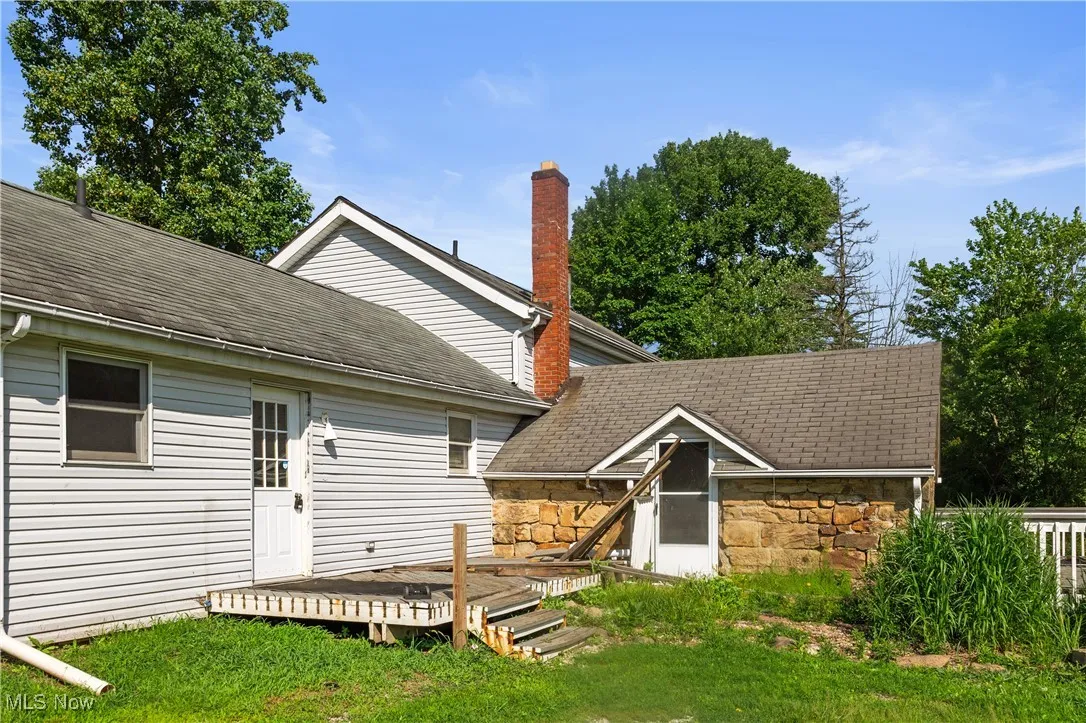 Back of house with a wooden deck, stone siding, and a lawn