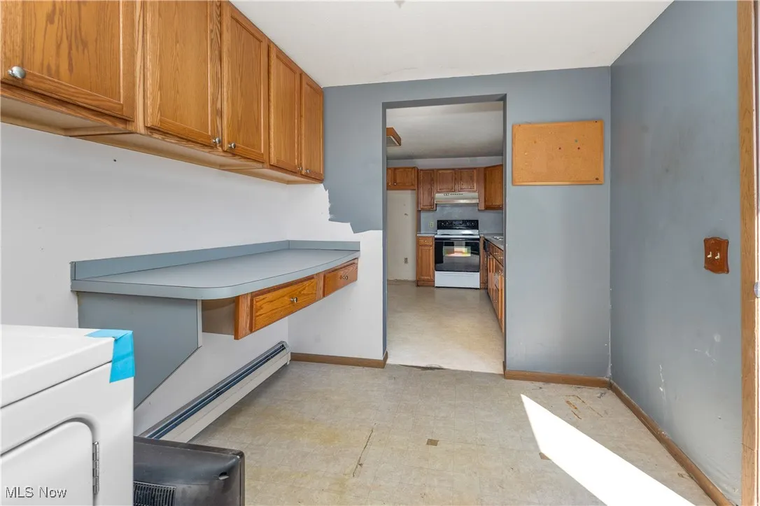 Kitchen featuring brown cabinets, washer / dryer, white electric range, and baseboard heating