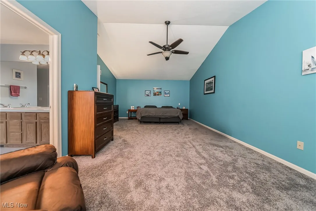 Bedroom featuring vaulted ceiling, carpet flooring, ceiling fan, and ensuite bath