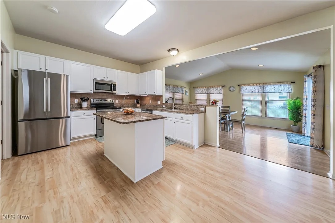 Kitchen featuring appliances with stainless steel finishes, lofted ceiling, light wood-type flooring, tasteful backsplash, and white cabinetry