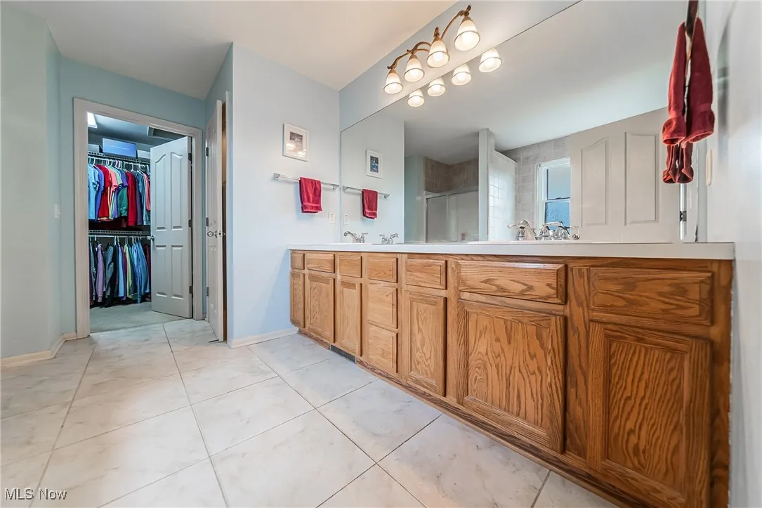 Bathroom featuring double vanity, a stall shower, a walk in closet, and tile patterned floors