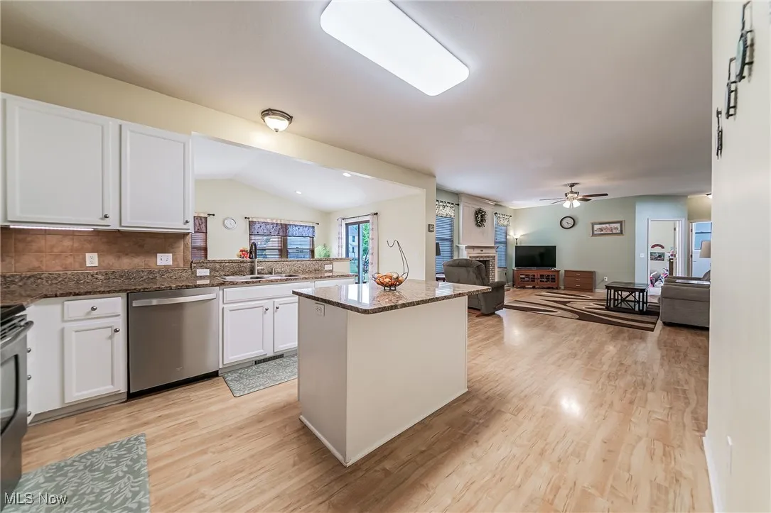 Kitchen featuring vaulted ceiling, appliances with stainless steel finishes, white cabinetry, a fireplace, and open floor plan