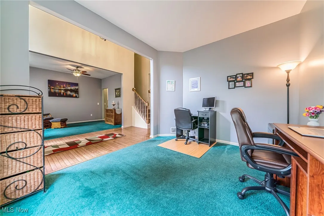 Carpeted home office featuring ceiling fan and wood finished floors